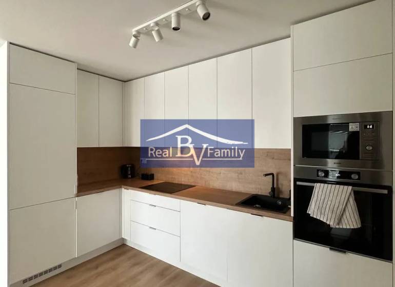 A kitchen in a 2-room apartment with a wooden decor floor, white cabinets, and built-in appliances.