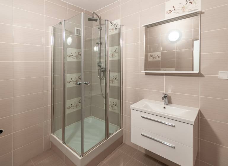 Bathroom with a shower in a 3-room apartment, light tiles, mirror above the sink.