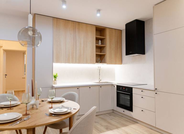 A kitchen in a 4-room apartment with white cabinets, wooden cupboards, and a small dining table.