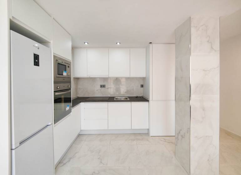 A kitchen in a 3-room apartment with white cabinets and built-in appliances, a floor with a marble appearance.