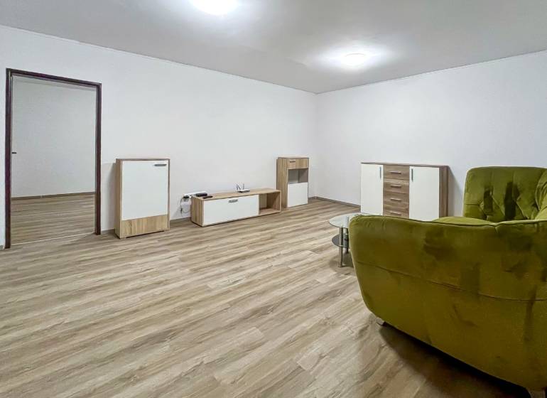 Living room of a two-room apartment with a wooden decor floor and a green armchair.