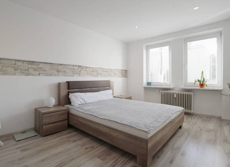 A bedroom in a two-room apartment with a bed, windows, and a floor with a wooden decor.