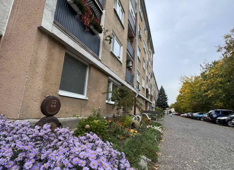 The exterior of an apartment building on SNP Street in Šahy with flowers and parked cars.