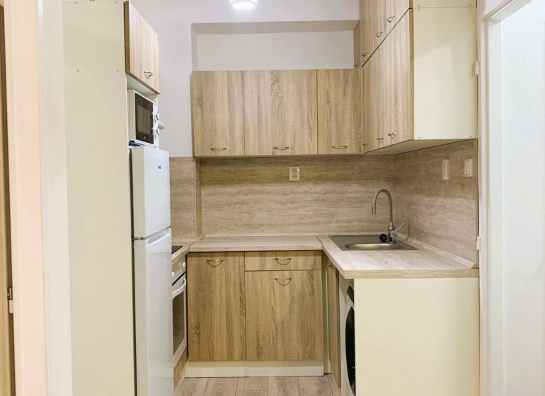 A kitchen in a 3-room apartment with wood-patterned flooring and light-colored furniture.
