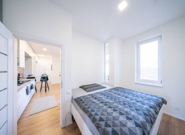 A bedroom in a two-room apartment with a wooden decor floor and a spacious bed.