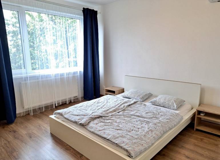 A bright bedroom with a large window, a bed, and a wooden decor floor in a 3-room apartment.