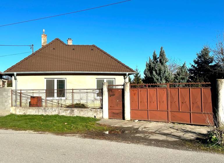 A family house in Horné Saliby with a gabled roof and a large metal gate.