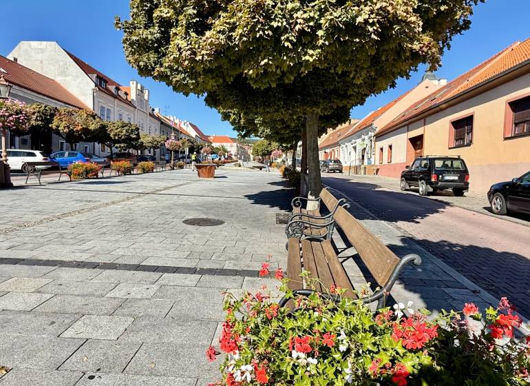 City park in the historic center of Svätý Jur on Prostredná Street with benches and trees.
