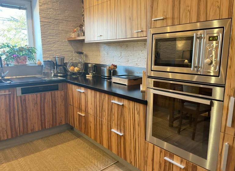 A kitchen with wooden cabinets, a built-in oven, and a window in a 2-room apartment.