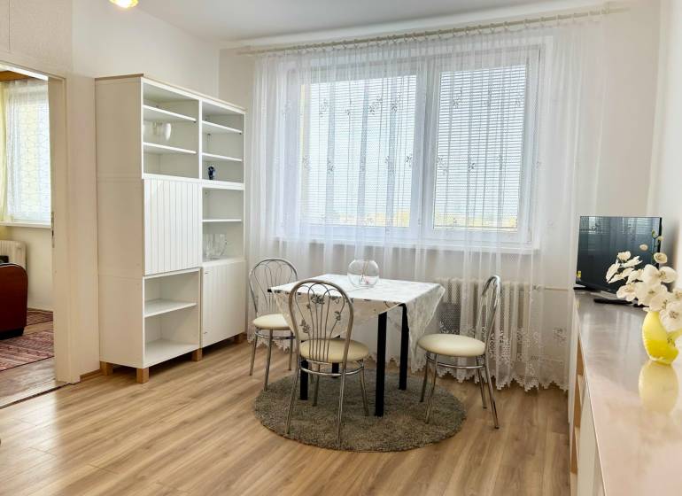 Dining room in a 2-room apartment with wood-patterned flooring and white furniture.
