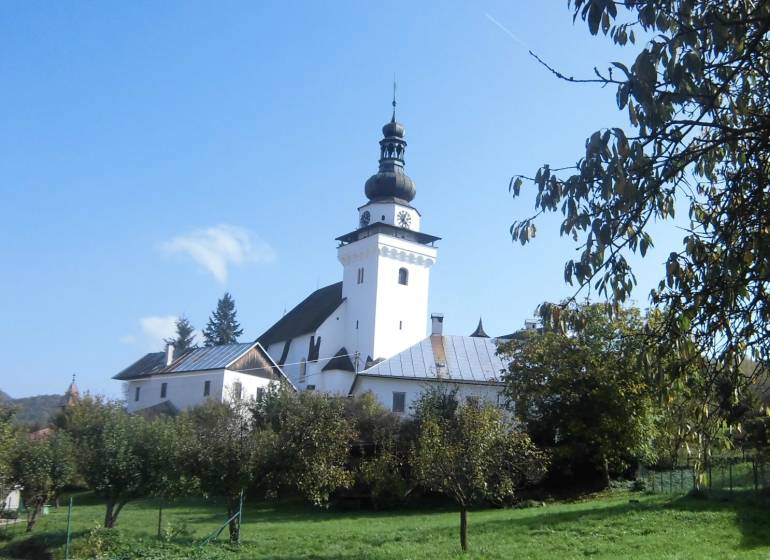 A church in Dubové surrounded by trees under a blue sky on a hillside.
