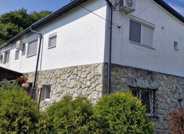 A stone house with a white facade surrounded by greenery in Hollóháza.