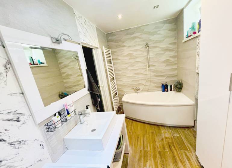 A bathroom in a 3-room apartment with a corner bathtub and a floor with a wood design.