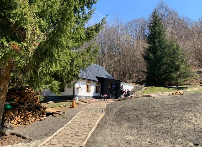A cottage surrounded by forest in the village of Píla with a footpath and stored wood.
