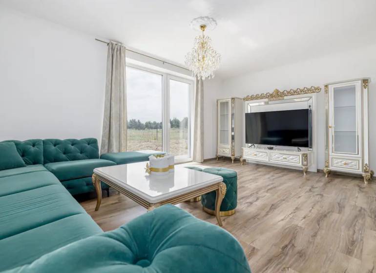 A spacious living room in a family house with a corner sofa and a wooden-patterned floor.