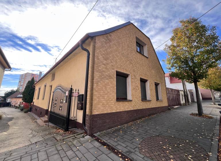 A house in Bratislava-Rača with a sloped roof, interlocking pavement, and trees along the walkway.
