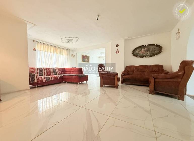 A bright living room in a family house with tiles, a red sofa, and brown armchairs.
