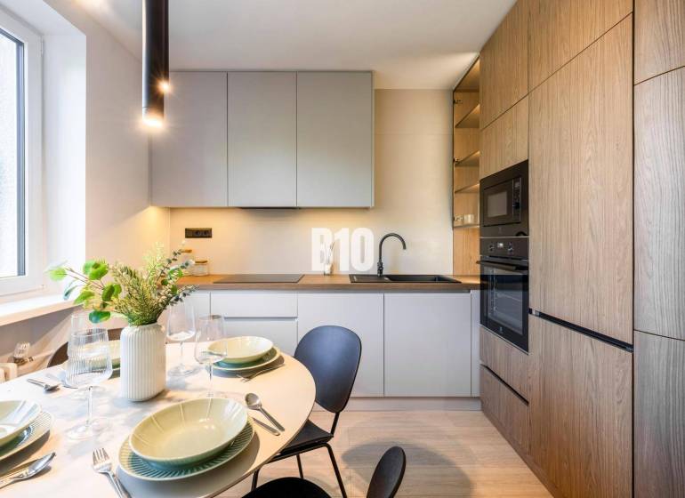 A kitchen of a 3-room apartment with a dining table and a wooden-patterned floor.