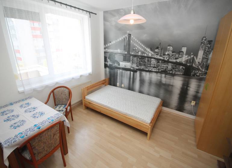 A room with a bed, a table, and a photo wallpaper of a bridge in a studio apartment, with a floor featuring a wooden decor.