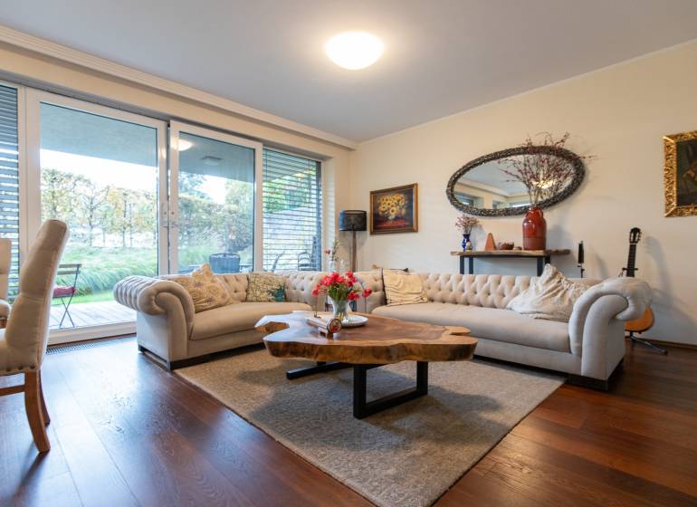 Living room in a three-room apartment with a wood-patterned floor and a large window.