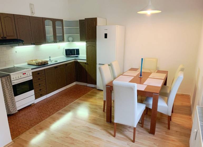 A kitchen in a 2-room apartment with a dining table, wooden cabinets, and a wooden decor floor.