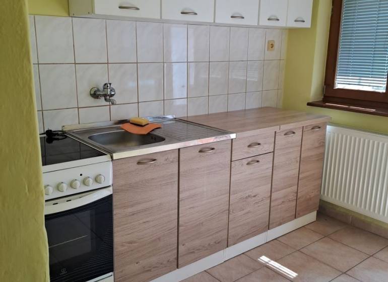 A kitchen in a studio apartment with white cabinets and tiled flooring.