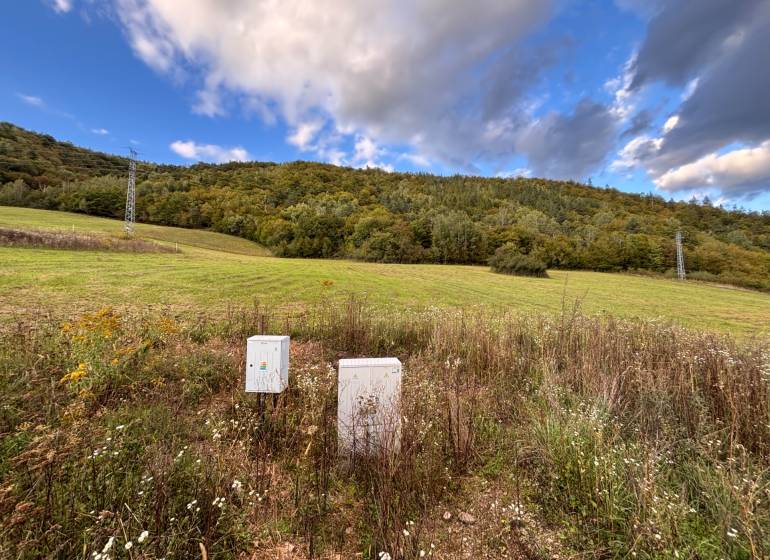 Greenery and control cabinets on a residential plot in Margecany surrounded by hills.