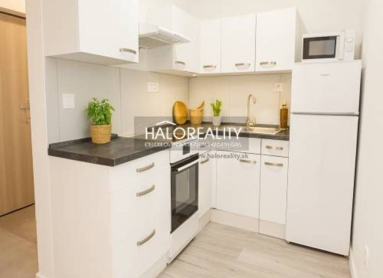A kitchen in a studio apartment with white cabinets and a wood-patterned floor.