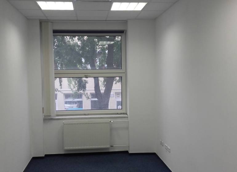 White office with a window, radiator, and blue carpet.