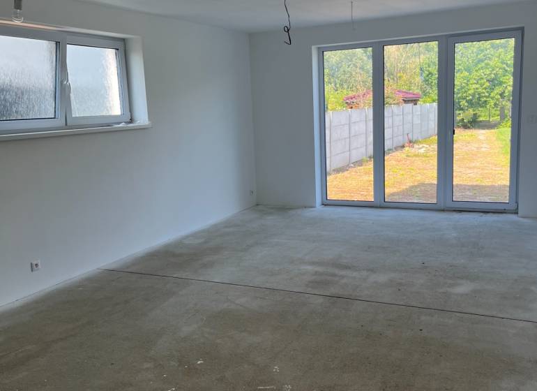 Empty room in a family house with a concrete floor and a large window to the garden.