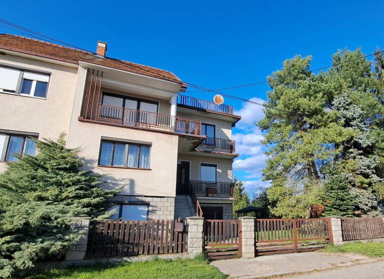 A family house in Hronské Kosihy, with two balconies, a garden, and trees on the property.