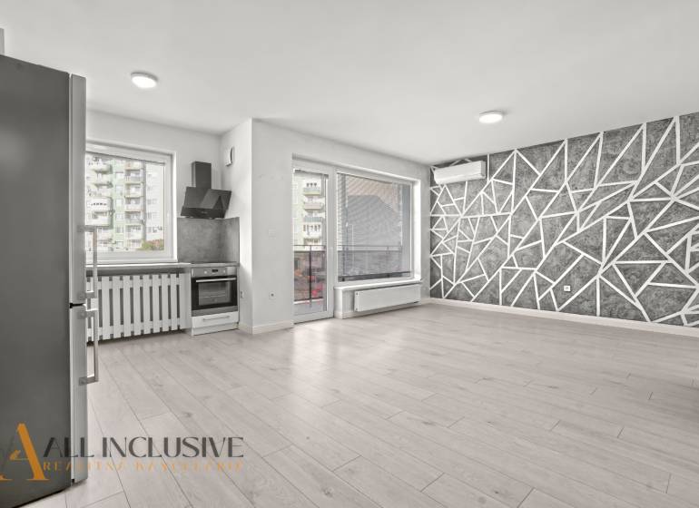 Kitchen and living room in a 2-room apartment with a wooden decor floor and a geometric wall.