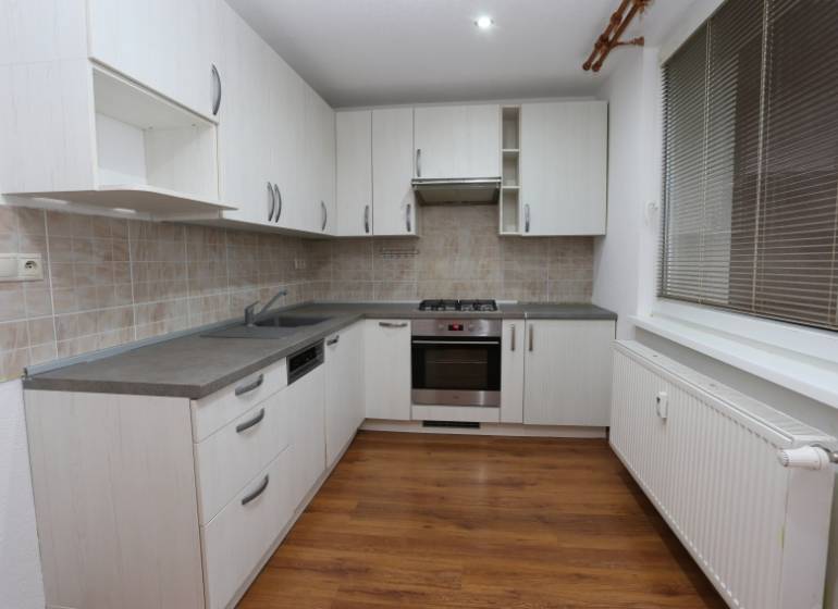 A kitchen in a 3-room apartment with white cabinets and a wood-patterned floor.