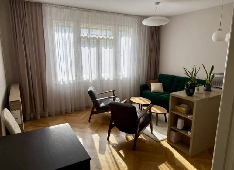 Living room in a 3-room apartment with a wooden decor floor, green sofa, wooden chairs.