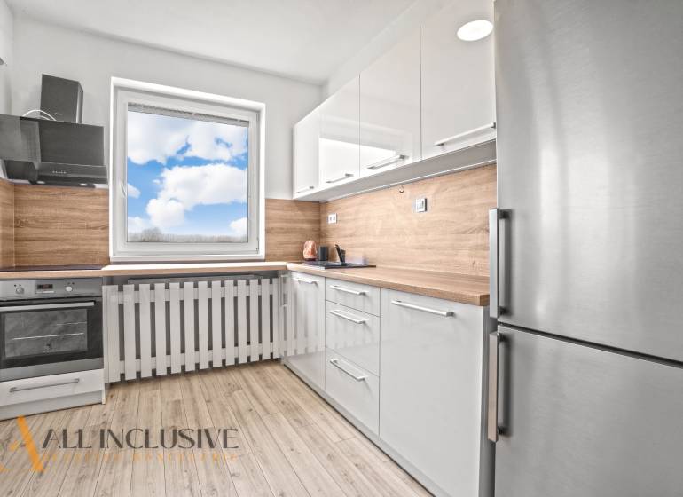 White kitchen in a 2-room apartment with wood-patterned flooring and a view from the window.