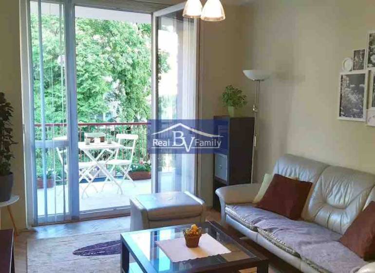 Living room in a 2-room apartment with a spacious balcony and a view of greenery.
