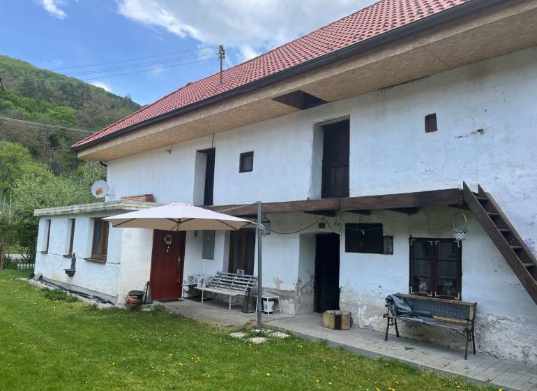 A country cottage with a red roof and a terrace, surrounded by a green lawn and nature.