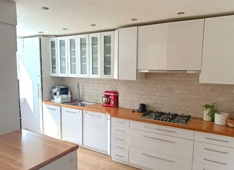 A kitchen in a 3-room apartment with white furniture and a stove, flooring with a wooden decor.