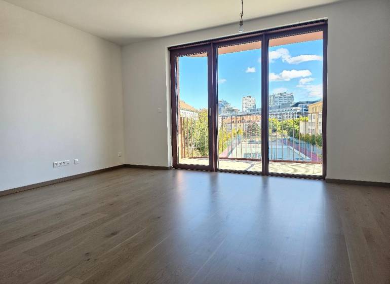 A spacious room with a wooden decor floor and a large window in a studio apartment.