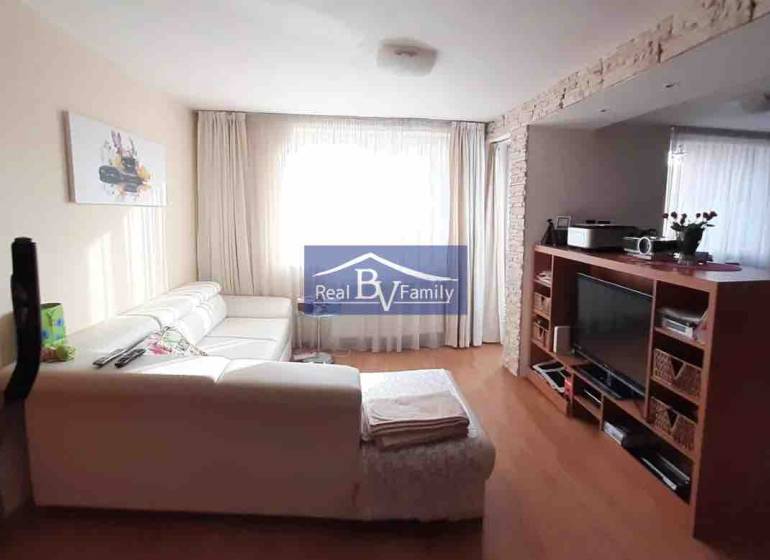 Living room with a white sofa and a television, wooden decor flooring, 2-room apartment.