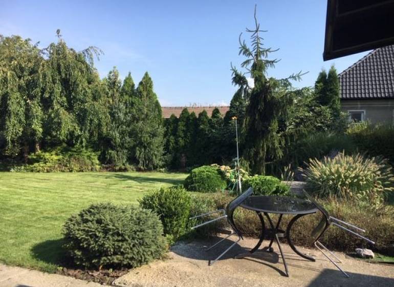 The garden of a family house in Čierna Voda with a lawn, trees, and outdoor seating.
