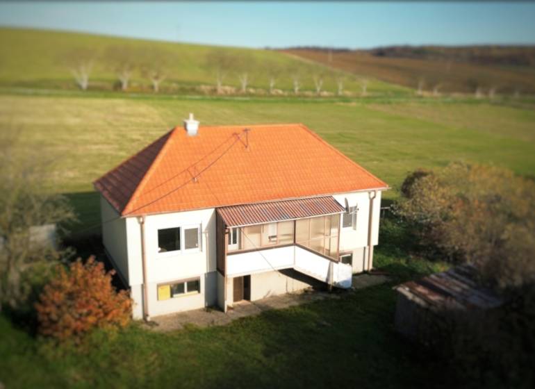 A family house in Dobrá Voda with a sloped roof, surrounded by greenery and meadows.