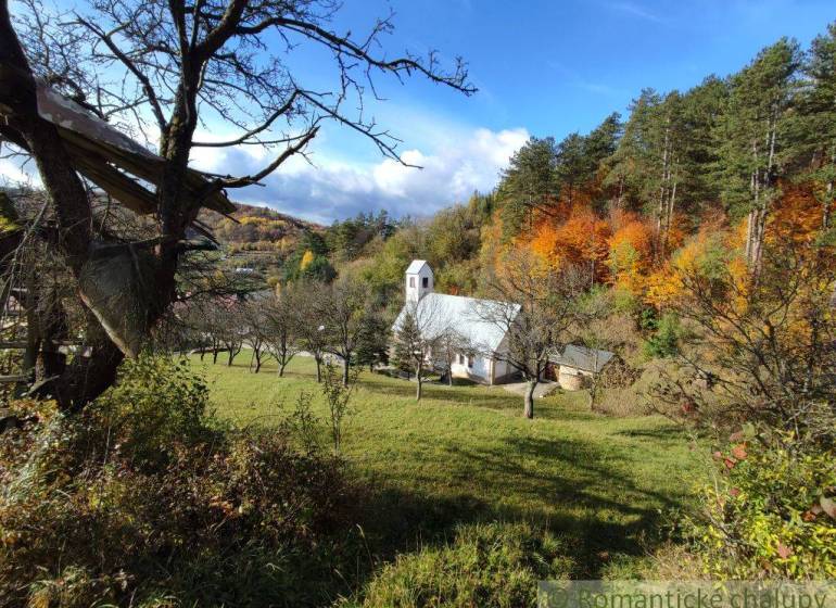 Autumn in the gardens of Hlboké nad Váhom with a small church among the trees, colorful forests in the background.