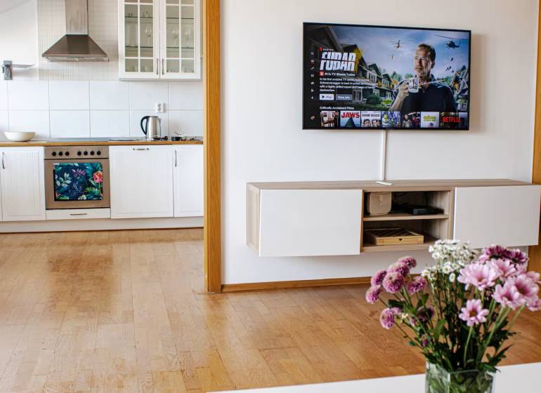 A kitchen in a 3-room apartment with a TV on the wall and flowers on the table.