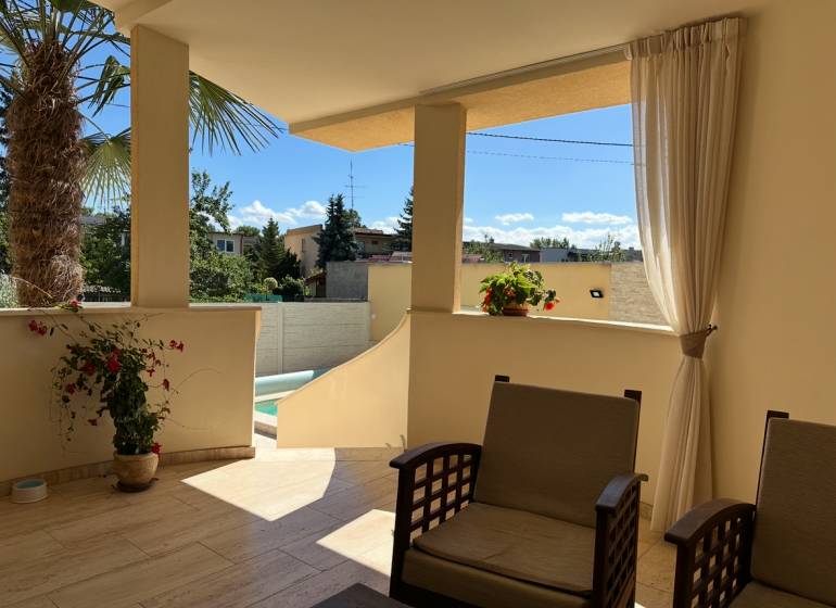The terrace of a family house in Komárno with seating and a view of the yard with a palm tree.