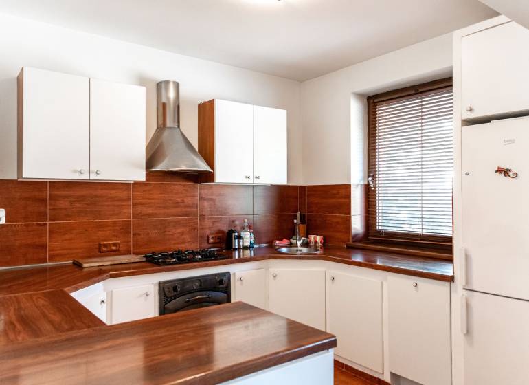 A kitchen with white cabinets, brown tiles, and a dark workspace in a two-room apartment.