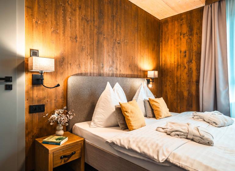 A bedroom with wooden paneling, a comfortable bed, and a side table in a two-room apartment.