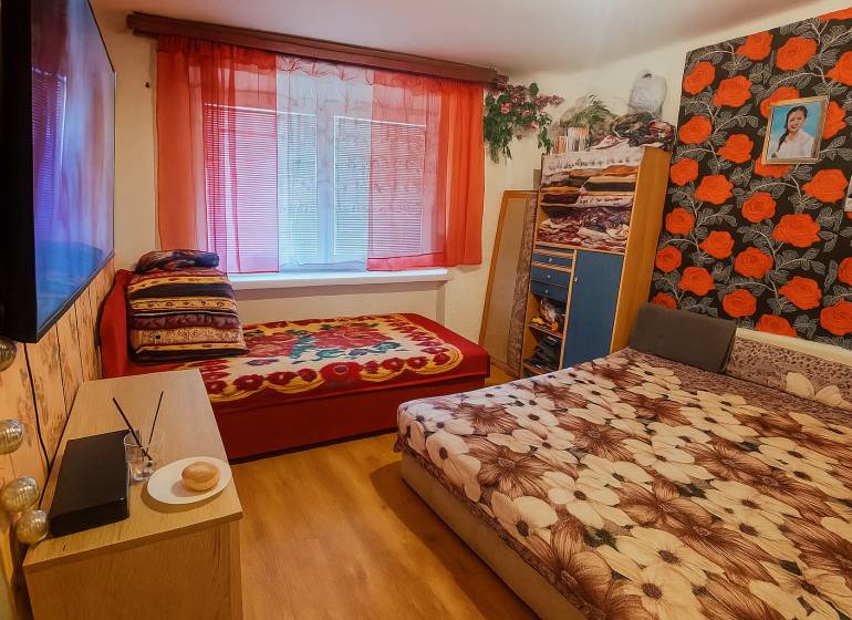 A bedroom in a two-room apartment with a wooden decor floor and colorful bed linens.