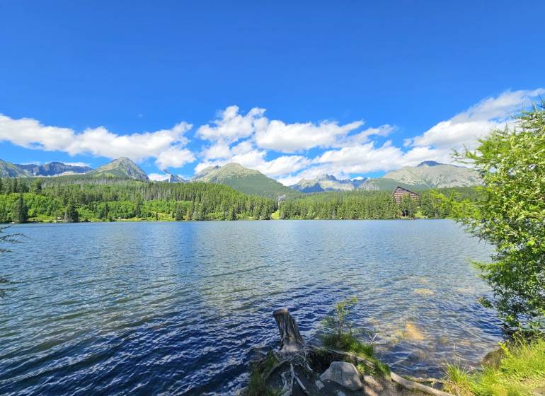 The lake in Štrba surrounded by agricultural and forest lands with mountains and a blue sky.