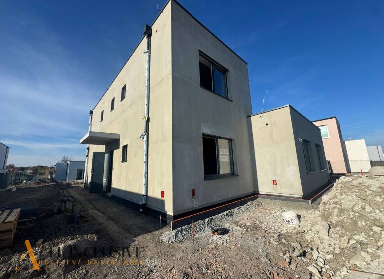 A family house under construction in Hubice, with a minimalist exterior and neighboring buildings.